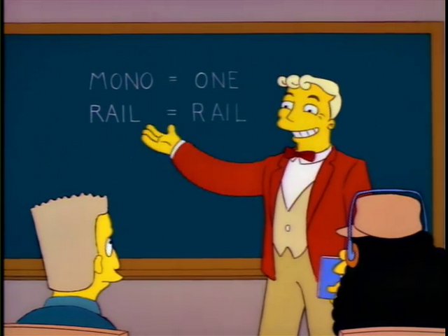 Lyle Lanley from The Simpsons monorail episode, standing in front of a chalkboard smiling and pointing to the text, “Mono means one, rail means rail.”