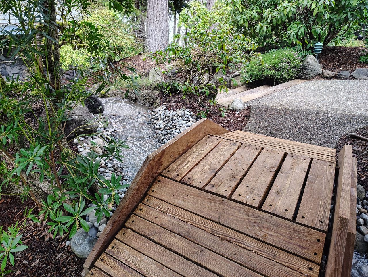 The same stream, this time looking from the bridge and downward towards the pond. there are plants on either side of the stream.